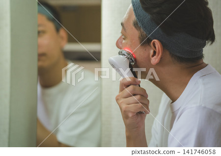 一名 40 歲的男子在浴室鏡子前使用多功能臉部護理儀按摩下巴,這是他日常護膚的一部分。 一名 40 歲的男子在浴室鏡子前使用多功能臉部護理儀按摩下巴,這是他日常護膚的一部分。 141746058