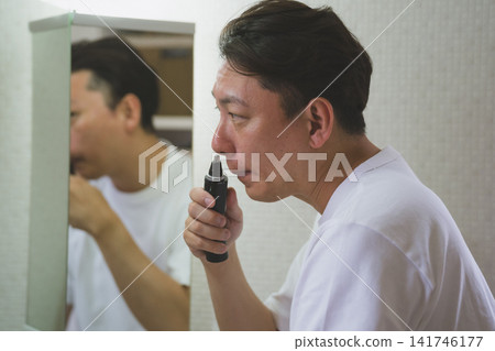 A man in his 40s using a nose trimmer in front of the bathroom mirror. A man in his 40s using a nose trimmer in front of the bathroom mirror. 141746177