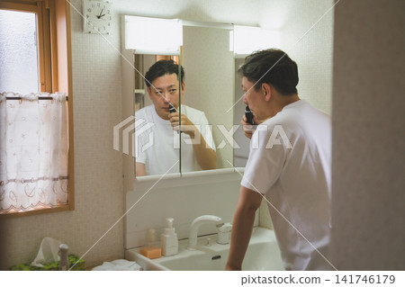 A man in his 40s trims his nose hairs while looking at his reflection in the bathroom mirror. A man in his 40s trims his nose hairs while looking at his reflection in the bathroom mirror. 141746179