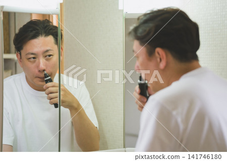 A 40-year-old man trimming his nose hairs, as seen in the bathroom mirror. A 40-year-old man trimming his nose hairs, as seen in the bathroom mirror. 141746180