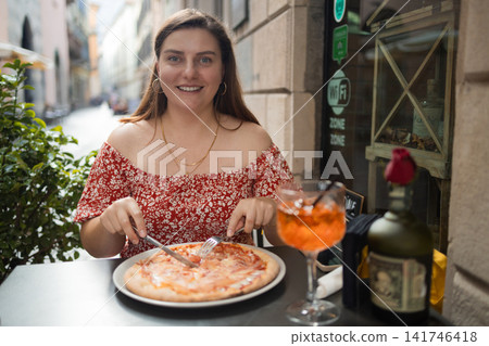 Happy young woman eating delicious Italian pizza at outdoor cafe in Europe Happy young woman eating delicious Italian pizza at outdoor cafe in Europe 141746418