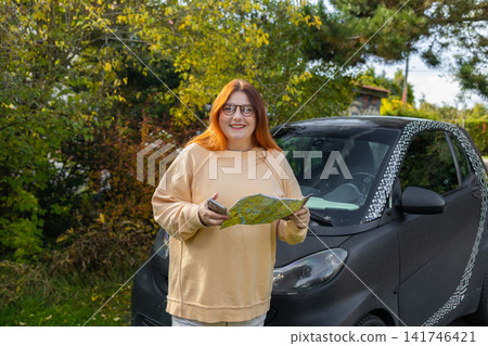 Woman holding map and using smartphone near car on road trip Woman holding map and using smartphone near car on road trip 141746421