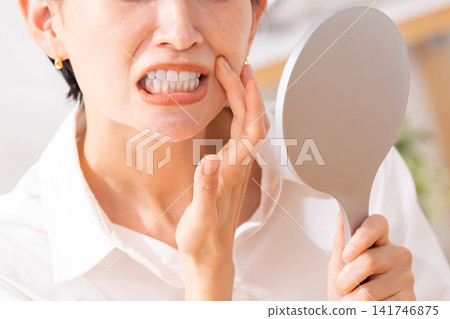 A woman is concerned about her gums and toothache while looking in the mirror. A woman is concerned about her gums and toothache while looking in the mirror. 141746875