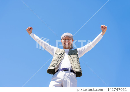 A man in work clothes strikes a victory pose against a blue sky. A man in work clothes strikes a victory pose against a blue sky. 141747031