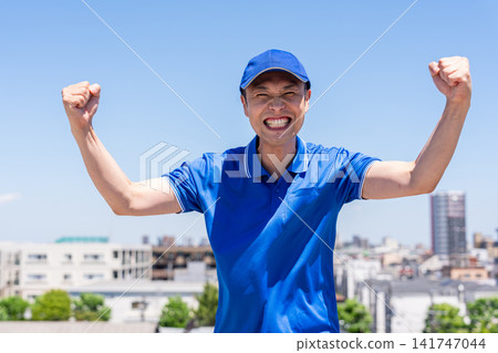 A male truck driver strikes a victory pose against a blue sky. A male truck driver strikes a victory pose against a blue sky. 141747044