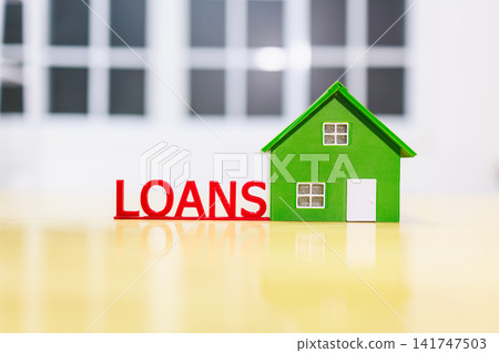 A small green house model beside red loans letters, home financing, mortgage and property buying concept on a bright indoor background. 141747503