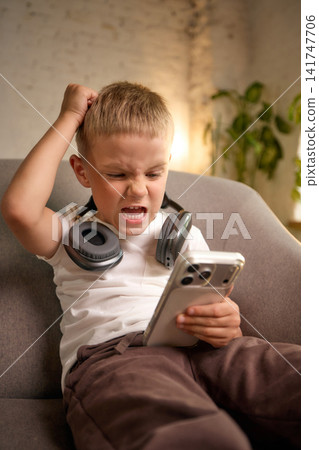 Frustrated five-year-old boy reacting emotionally to smartphone content. Frustrated five-year-old boy reacting emotionally to smartphone content. 141747706