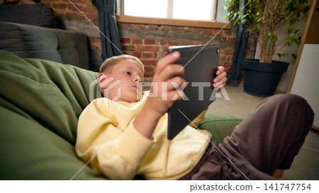 Five-year-old boy reclining with tablet during casual leisure time at home. Five-year-old boy reclining with tablet during casual leisure time at home. 141747754