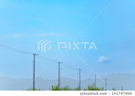 A nostalgic scene of utility poles and power lines stretching against a backdrop of blue sky and distant mountain ranges. A nostalgic scene of utility poles and power lines stretching against a backdrop of blue sky and distant mountain ranges. 141747969
