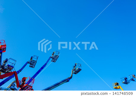 A low-angle, graphic composition capturing a cluster of cherry picker crane arms extending dynamically into a clear blue sky. A low-angle, graphic composition capturing a cluster of cherry picker crane arms extending dynamically into a clear blue sky. 141748509