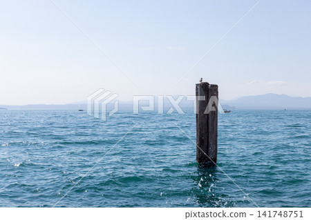 Solitary mooring post in open blue Lake Garda water near Lazise in summer daylight Solitary mooring post in open blue Lake Garda water near Lazise in summer daylight 141748751