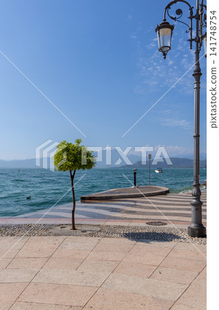 Lakeside promenade in Lazise curving beside turquoise Lake Garda water Lakeside promenade in Lazise curving beside turquoise Lake Garda water 141748754