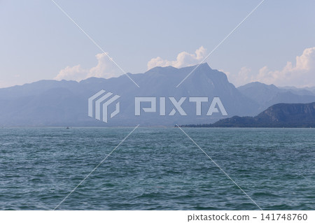Lake Garda and layered Alpine mountains seen from the Lazise shore in summer Lake Garda and layered Alpine mountains seen from the Lazise shore in summer 141748760