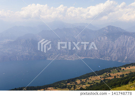 Lake Garda mountain view from Monte Baldo with a small paraglider in the sky Lake Garda mountain view from Monte Baldo with a small paraglider in the sky 141748778