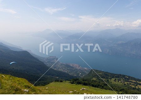 Lake Garda and a lakeside town below Monte Baldo with a distant paraglider Lake Garda and a lakeside town below Monte Baldo with a distant paraglider 141748780