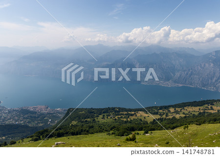 Sunny Monte Baldo meadow above Lake Garda, shoreline towns and rugged mountains 141748781