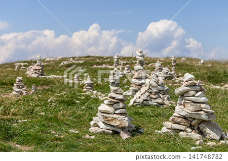 Stone cairns scattered across a sunny Monte Baldo meadow beneath white clouds Stone cairns scattered across a sunny Monte Baldo meadow beneath white clouds 141748782