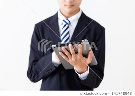 A young businessman in a suit holding a tablet. A young businessman in a suit holding a tablet. 141748948