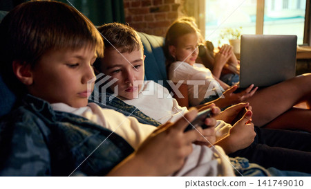 Boys using smartphones while another child works on laptop in background Boys using smartphones while another child works on laptop in background 141749010
