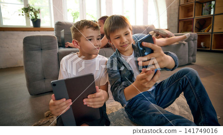 Two boys sharing digital content between smartphone and tablet on sofa Two boys sharing digital content between smartphone and tablet on sofa 141749016
