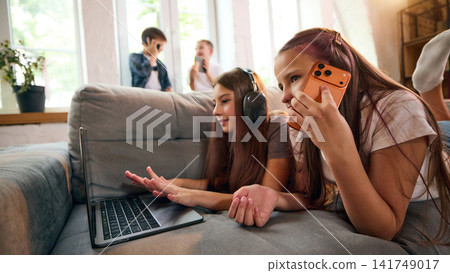 Girls multitasking between smartphone conversation and laptop at home Girls multitasking between smartphone conversation and laptop at home 141749017