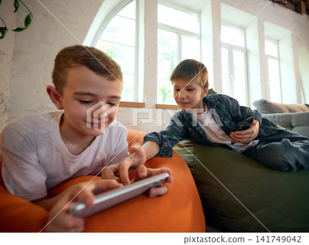 Two school-age boys playing mobile games together on smartphones at home Two school-age boys playing mobile games together on smartphones at home 141749042