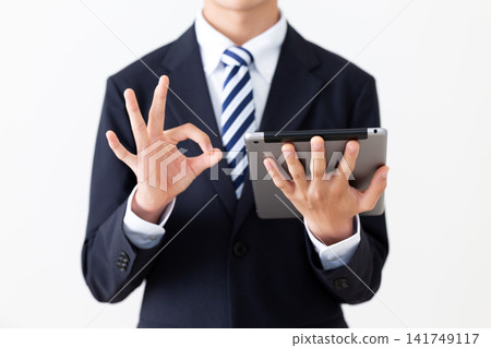 A young businessman in a suit makes a circular motion while holding a tablet. A young businessman in a suit makes a circular motion while holding a tablet. 141749117
