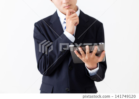 畫面中,一位身穿西裝的年輕商人神情憂慮,手裡拿著一台平板電腦。 畫面中,一位身穿西裝的年輕商人神情憂慮,手裡拿著一台平板電腦。 141749120