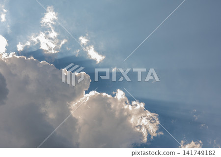 Sun rays breaking through dramatic white clouds in bright blue sky Sun rays breaking through dramatic white clouds in bright blue sky 141749182