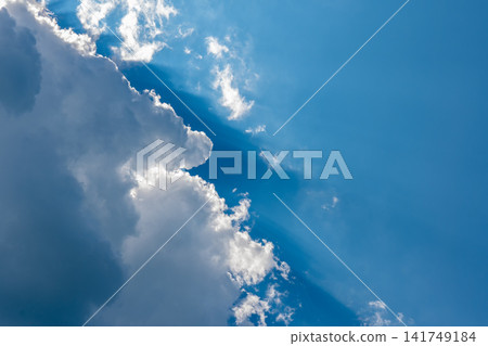 Sunlight beams through towering white clouds against a vivid blue sky Sunlight beams through towering white clouds against a vivid blue sky 141749184