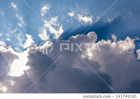Sunbeams breaking through towering storm clouds in a vivid blue sky Sunbeams breaking through towering storm clouds in a vivid blue sky 141749185