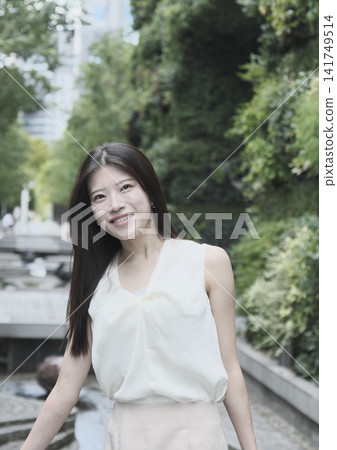 一位身穿無袖連身裙的年輕女子在綠樹成蔭的公園裡微笑。 一位身穿無袖連身裙的年輕女子在綠樹成蔭的公園裡微笑。 141749514