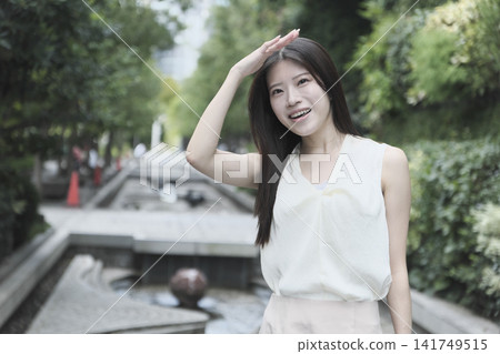一位身穿無袖連身裙的年輕女子在綠樹成蔭的公園裡微笑。 一位身穿無袖連身裙的年輕女子在綠樹成蔭的公園裡微笑。 141749515