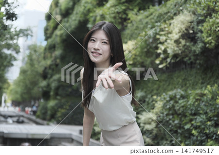 一位身穿無袖連身裙的年輕女子在綠樹成蔭的公園裡微笑。 一位身穿無袖連身裙的年輕女子在綠樹成蔭的公園裡微笑。 141749517