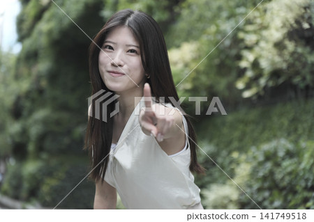 A young woman in a sleeveless dress smiles in a lush green park. A young woman in a sleeveless dress smiles in a lush green park. 141749518