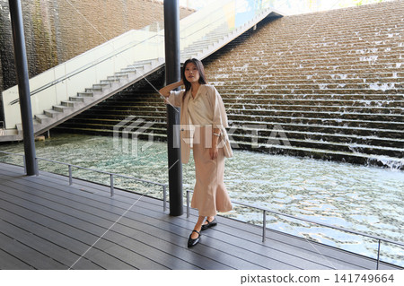 一位身著休閒職業裝的年輕女子在市中心的海濱廣場上微笑。 一位身著休閒職業裝的年輕女子在市中心的海濱廣場上微笑。 141749664