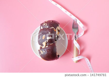 A measuring tape with fork and Bread topping with chocolate and almond on white dish. A measuring tape with fork and Bread topping with chocolate and almond on white dish. 141749781