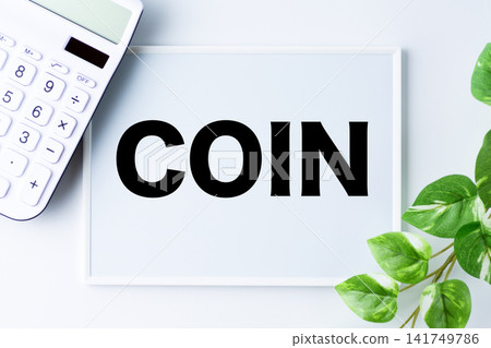 A whiteboard with the word "COIN" written on it and a white calculator. A whiteboard with the word "COIN" written on it and a white calculator. 141749786