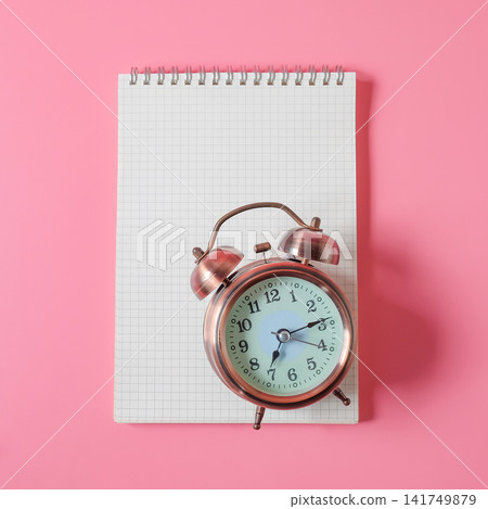 Vintage alarm clock lay on notebook on color background. Vintage alarm clock lay on notebook on color background. 141749879