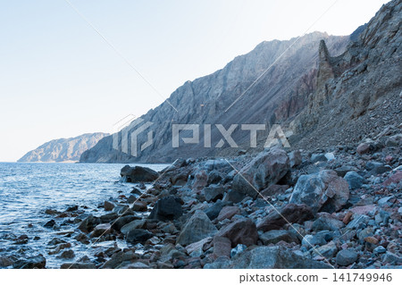 Coastal view of Dahab, Egypt, featuring the Red Sea and Sinai mountains. Rocky shoreline with clear water and distant mountains. Coastal view of Dahab, Egypt, featuring the Red Sea and Sinai mountains. Rocky shoreline with clear water and distant mountains. 141749946