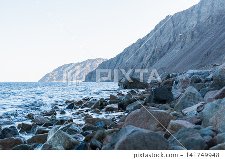 Coastal view of Dahab, Egypt, featuring the Red Sea and Sinai mountains. Rocky shoreline with clear water and distant mountains. Coastal view of Dahab, Egypt, featuring the Red Sea and Sinai mountains. Rocky shoreline with clear water and distant mountains. 141749948
