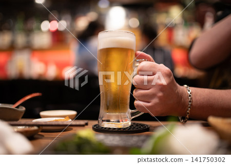 A man's hands holding a cold draft beer in an izakaya (Japanese pub) A man's hands holding a cold draft beer in an izakaya (Japanese pub) 141750302