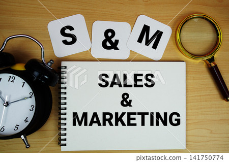 S and M Sales and Marketing text written on notepad with magnifying glass and alarm clock on wooden background S and M Sales and Marketing text written on notepad with magnifying glass and alarm clock on wooden background 141750774