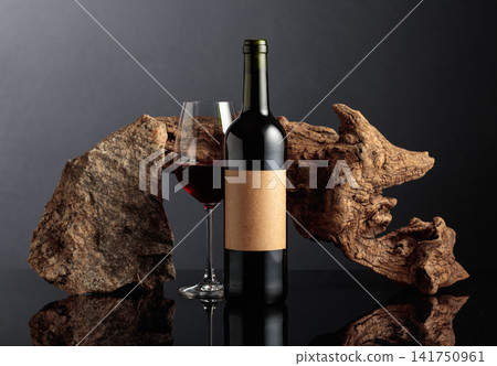 Red wine with old driftwood and a piece of granite rock on a black reflective background. Red wine with old driftwood and a piece of granite rock on a black reflective background. 141750961