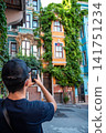 Istanbul, turkey, august 2, 2025 man holding smartphone, photographing vibrant, ivy covered historical houses in balat, istanbul, experiencing culture and travel 141751234