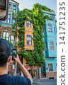 Istanbul, turkey, august 2, 2025 man documenting vibrant historic houses covered with green climbing plants in balat district, istanbul, turkey. Urban travel concept 141751235