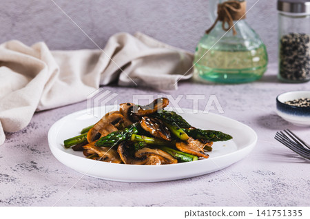 Vegetarian fried asparagus and mushrooms with sesame seeds on a plate on the table Vegetarian fried asparagus and mushrooms with sesame seeds on a plate on the table 141751335
