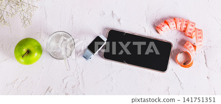A fitness tracker, smartphone, apple, dumbbells, and a glass of water on a table top view web banner 141751351