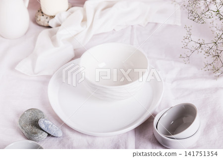 Coarse linen drapery for a kitchen table with ceramic dishes in white tones 141751354
