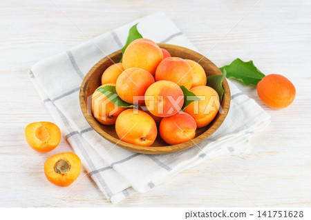Fresh apricots in wooden bowl with green leaves on white wooden background. Healhy food, ripe friut Fresh apricots in wooden bowl with green leaves on white wooden background. Healhy food, ripe friut 141751628
